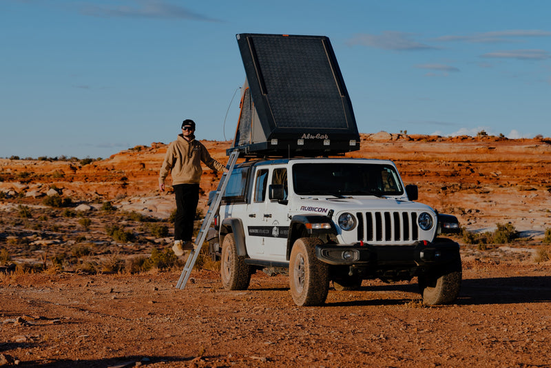 This 4x4 Jeep with a rooftop tent is an ideal RV rental for desert overlanding. Man on ladder, red rock backdrop. — photo 8