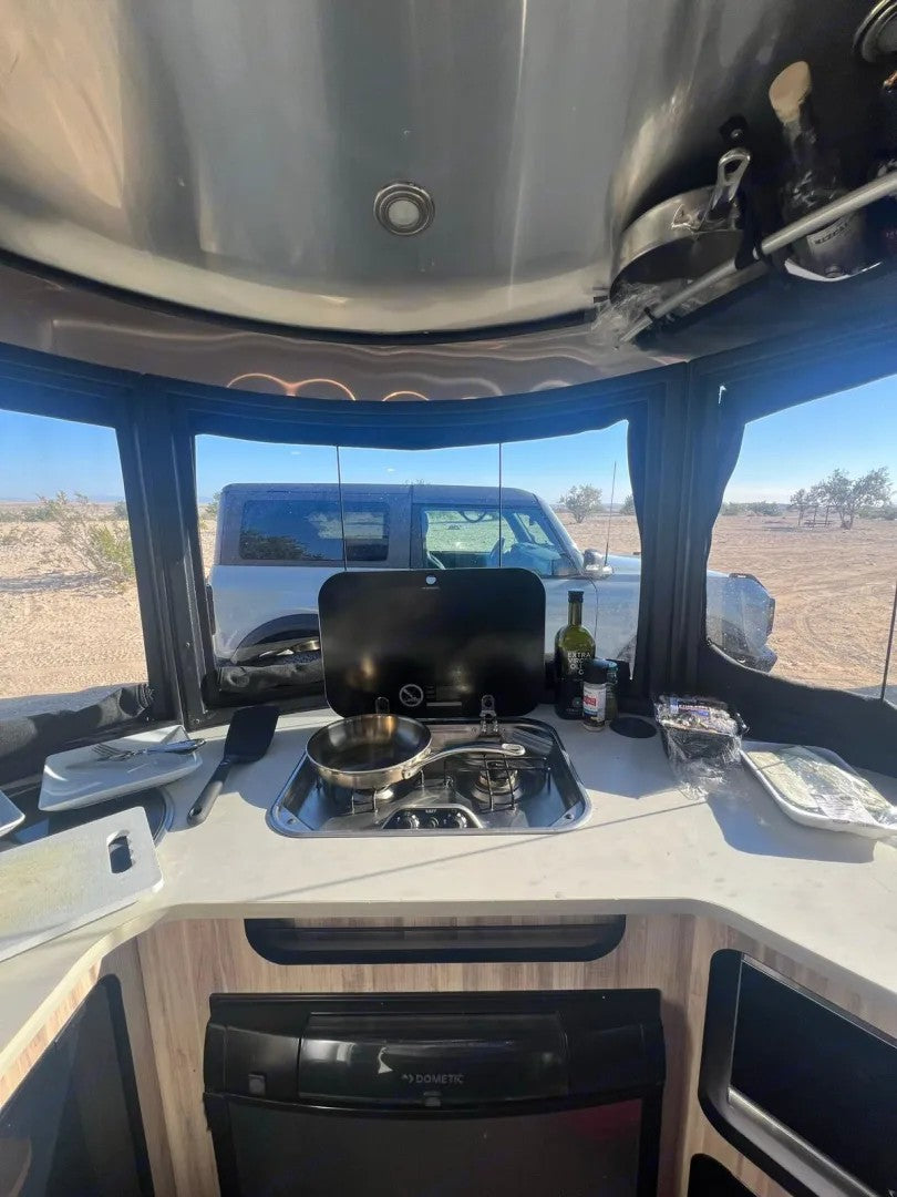 Interior of an RV kitchen with stove, fridge, and desert view. Bronco parked outside. Great for an rv rental adventure! — photo 3