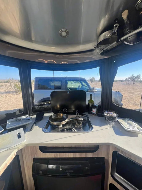 Interior of an RV kitchen with stove, fridge, and desert view. Bronco parked outside. Great for an rv rental adventure!