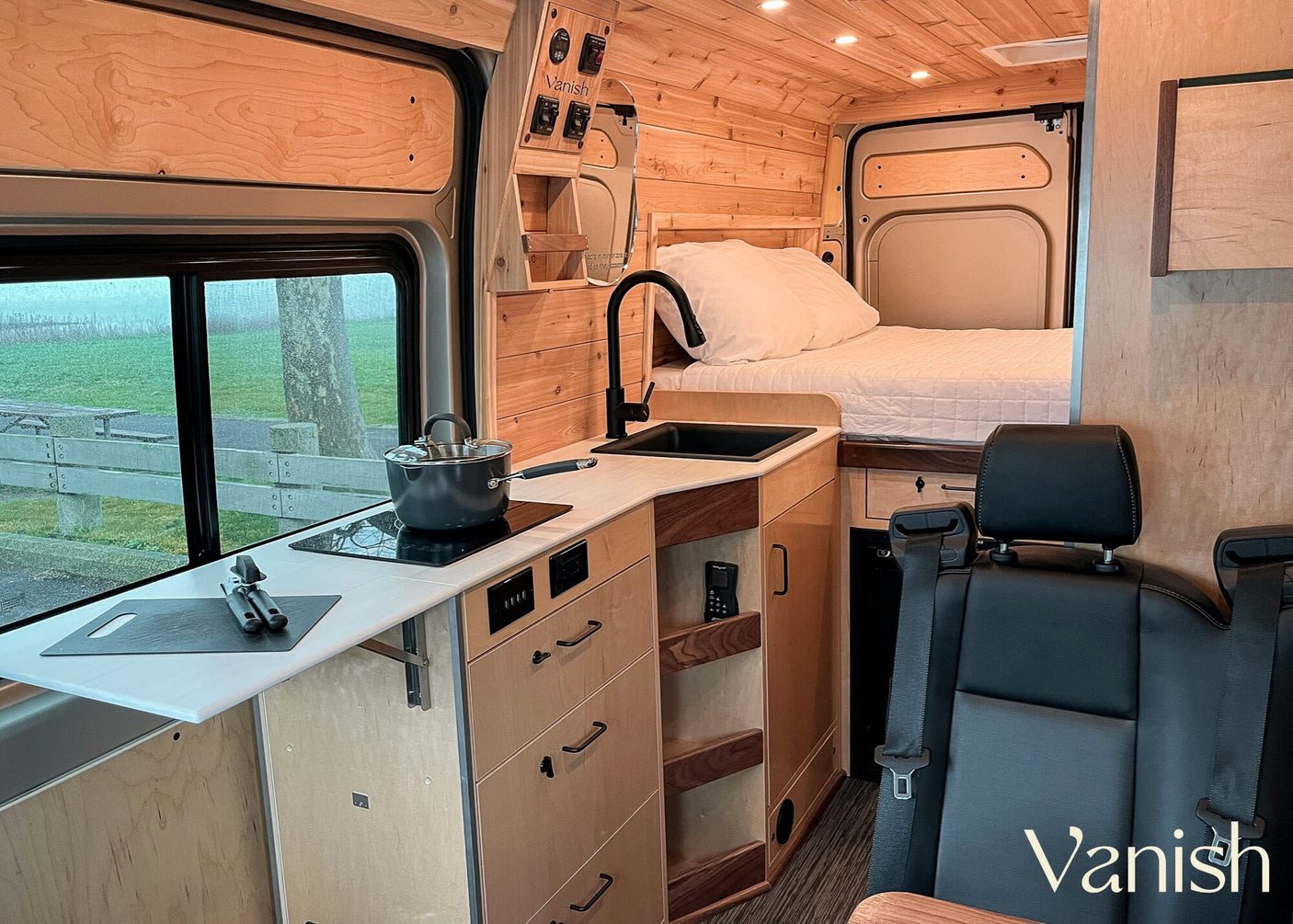 Interior of a modern RV rental, featuring a functional kitchen area, comfortable bed, and warm wood finishes.