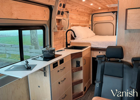Interior of a modern RV rental, featuring a functional kitchen area, comfortable bed, and warm wood finishes.