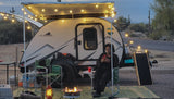Enjoying an RV rental adventure! A woman relaxes by a fire pit under string lights next to her travel trailer in the desert.