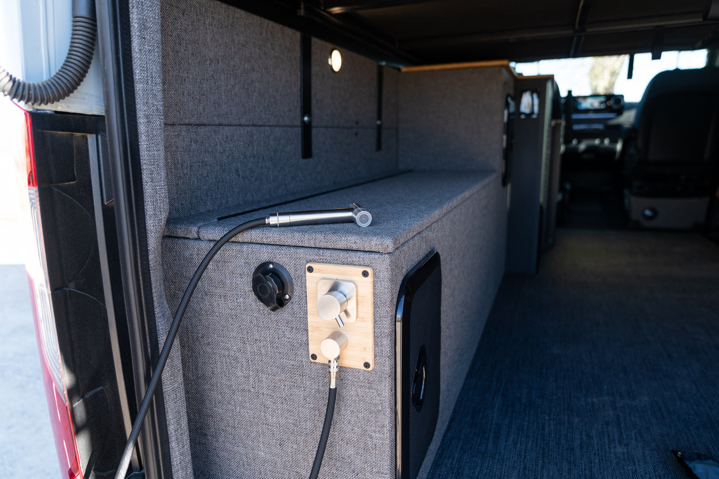 RV rental's rear utility area with a connected hose, shower nozzle, and water controls on gray fabric walls.