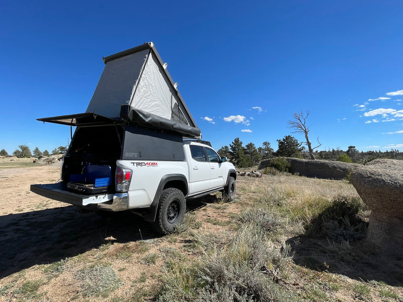 Ready for an RV rental trip? White truck camper with pop-top tent and open tailgate kitchen in a sunny, rugged landscape. — photo 5