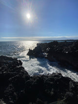 Sunlit ocean waves crash on dark volcanic rocks, creating a dramatic coastal scene. Perfect for your next RV rental adventure!