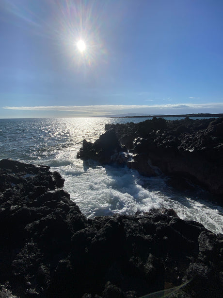 Sunlit ocean waves crash on dark volcanic rocks, creating a dramatic coastal scene. Perfect for your next RV rental adventure!