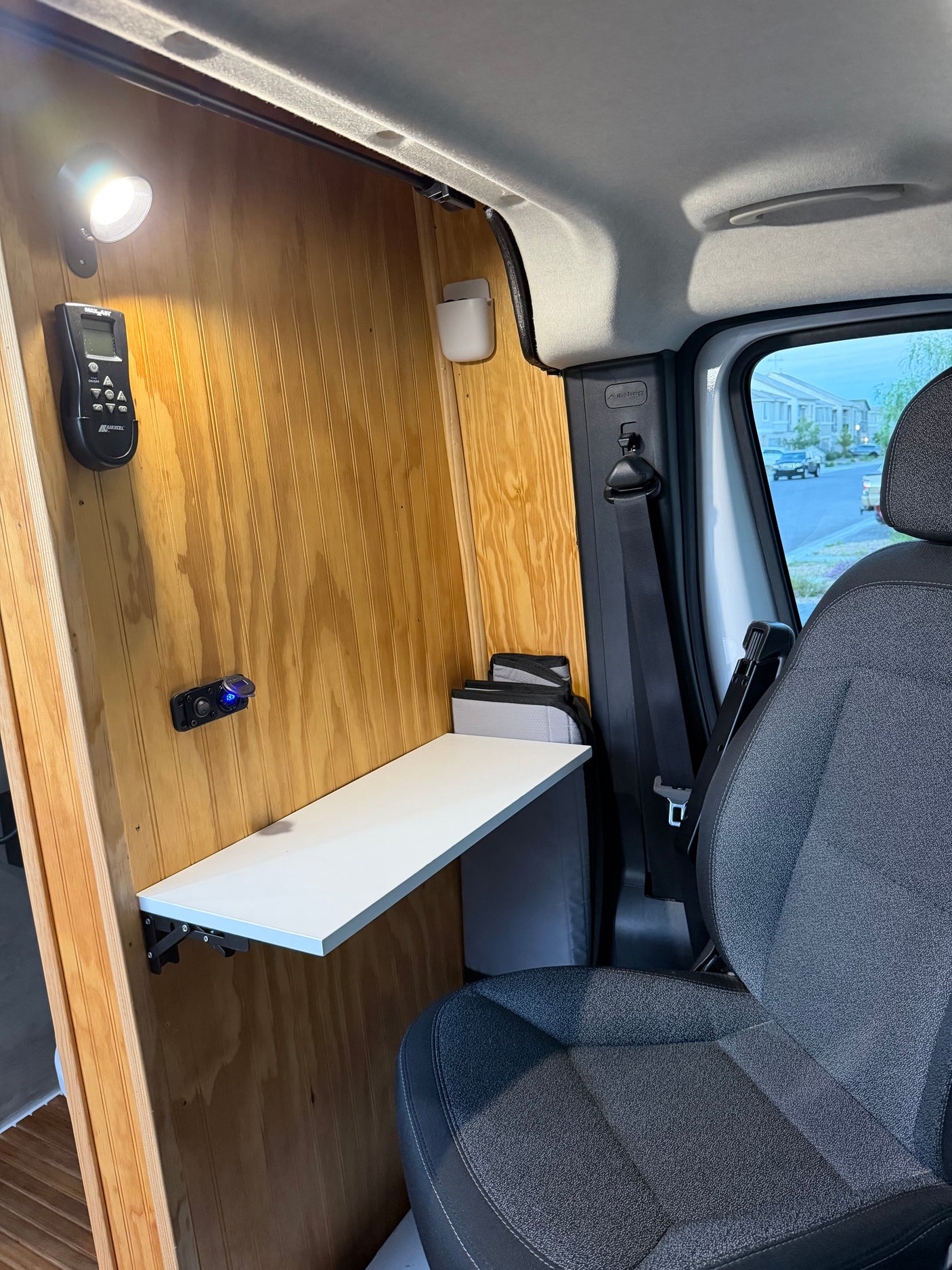 rv rental: Functional camper van interior with wooden walls, light, fold-down table, and power outlets by the passenger seat.