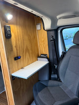 rv rental: Functional camper van interior with wooden walls, light, fold-down table, and power outlets by the passenger seat.
