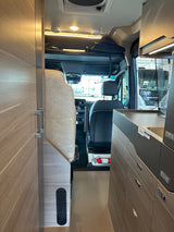 Inside a modern RV rental, featuring a functional kitchenette, cozy seating, and a view into the cockpit.