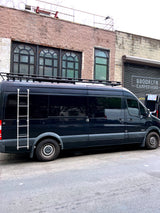 Black Mercedes Sprinter RV rental with roof rack and ladder, parked at Brooklyn Campervans, ready for adventure.