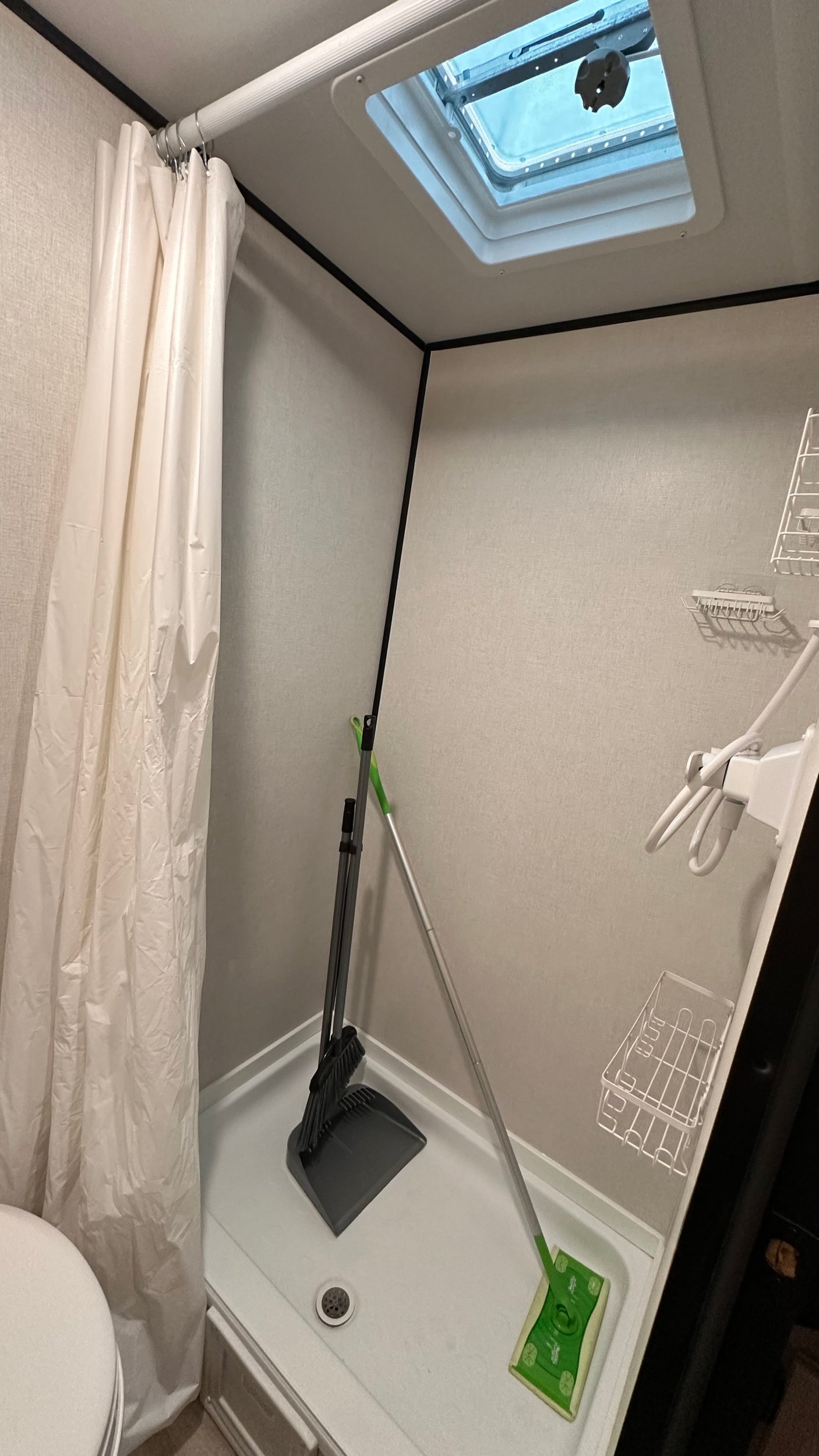 RV rental bathroom shower storing cleaning essentials (broom, dustpan, mop), featuring a curtain, vent, and shelving.