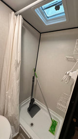 RV rental bathroom shower storing cleaning essentials (broom, dustpan, mop), featuring a curtain, vent, and shelving.