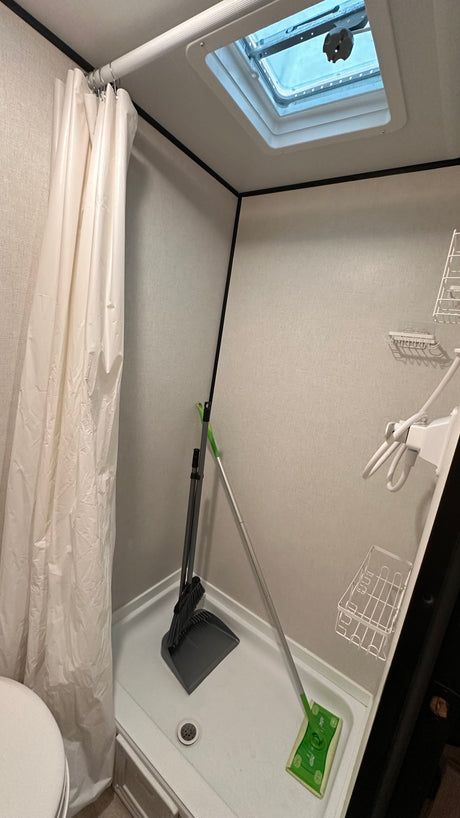 RV rental bathroom shower storing cleaning essentials (broom, dustpan, mop), featuring a curtain, vent, and shelving.
