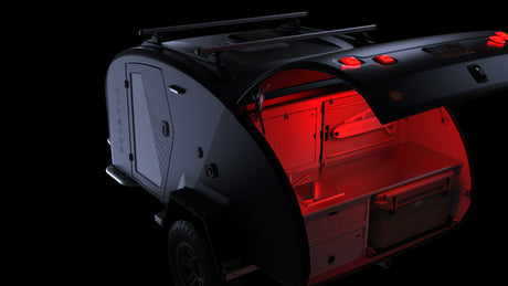 Dark grey Escapòd teardrop camper, perfect for RV rental, reveals a red-lit outdoor kitchen with YETI cooler.