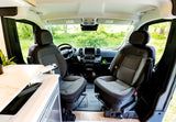 Explore this cozy rv rental's front cabin with comfortable swivel seats, dashboard, and a view of lush nature.