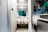 Bright & modern RV rental interior with a cozy bedroom, compact kitchen, & nature views. Ideal for travel!