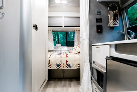 Bright & modern RV rental interior with a cozy bedroom, compact kitchen, & nature views. Ideal for travel!