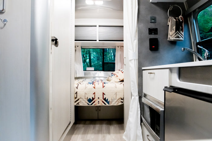 Bright & modern RV rental interior with a cozy bedroom, compact kitchen, & nature views. Ideal for travel!
