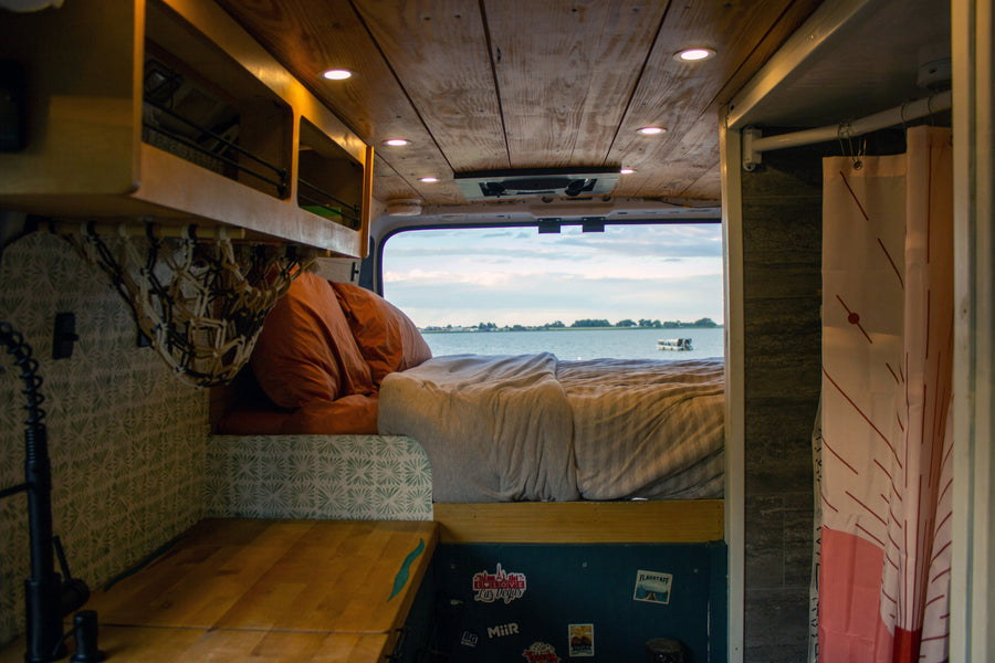 Cozy rv rental interior: a bed with rust-orange pillows faces a large window with a serene lake view and boat.