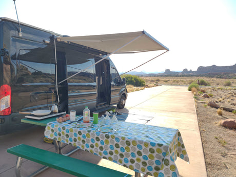 Enjoying a scenic rv rental breakfast outside a camper van with an extended awning in a desert landscape.