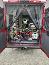 Red RV rental with open rear doors, showcasing interior bike storage and living area. Mesh screens visible for a camper van.
