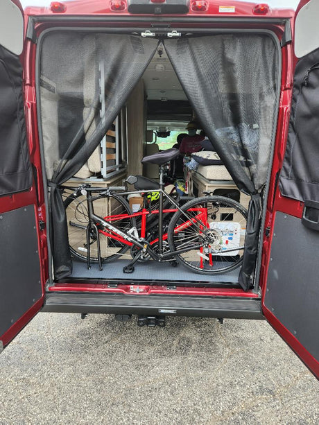 Red RV rental with open rear doors, showcasing interior bike storage and living area. Mesh screens visible for a camper van.
