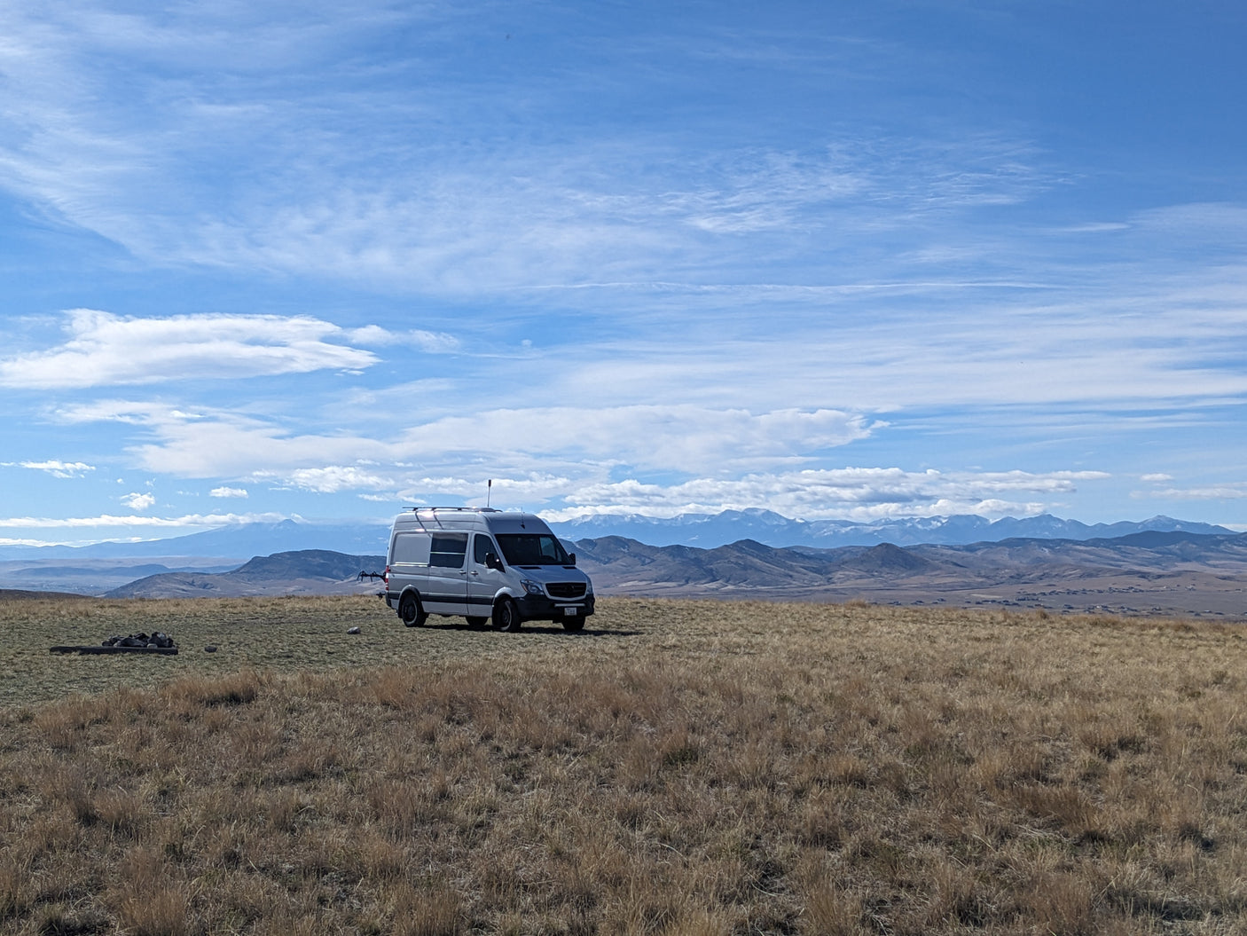 RV rental for remote adventures: A grey camper van on a vast, dry field with distant snowy mountains & blue sky.