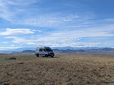 RV rental for remote adventures: A grey camper van on a vast, dry field with distant snowy mountains & blue sky.