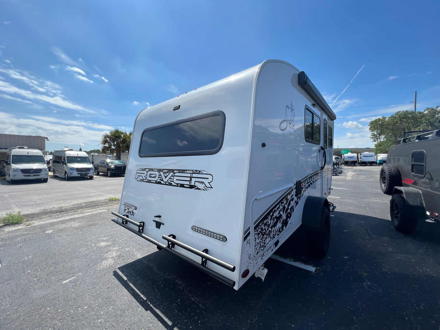 A modern white Sol Rover travel trailer, ideal for an RV rental, is showcased from the rear in a sunny outdoor lot.
