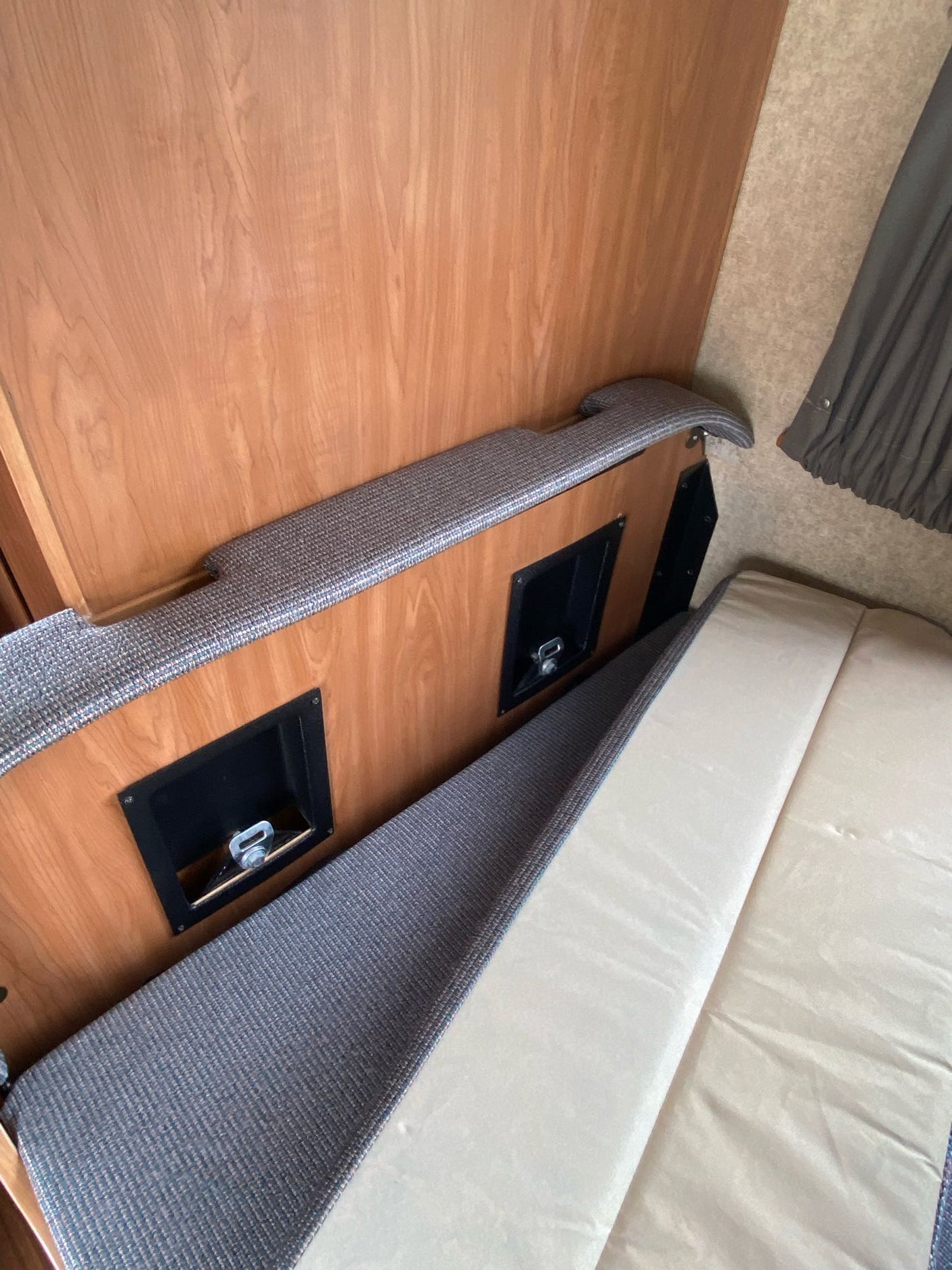 RV rental dinette converting to a bed. View shows wooden interior, gray upholstered base with tie-downs, and lifted mattress.