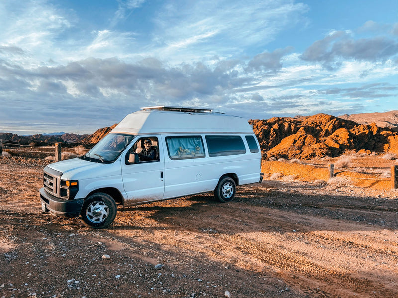 White van with high top, like an RV rental, parked on a dirt road in arid mountains under a dramatic sky. Person inside. — photo 11
