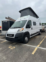 White Winnebago Solis pop-top RV rental (Ram ProMaster camper van) parked in lot 42 on a cloudy day.