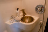 Compact RV rental wet bath featuring a bronze sink and faucet, hand soap, striped towels, and chrome shower controls.