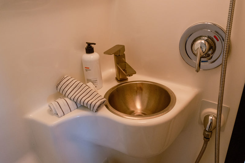 Compact RV rental wet bath featuring a bronze sink and faucet, hand soap, striped towels, and chrome shower controls. — photo 9