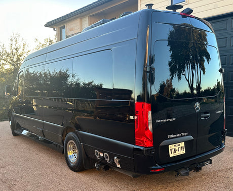 A sleek black Mercedes Sprinter camper van, possibly an rv rental, with visible hookups & a Dometic AC unit.