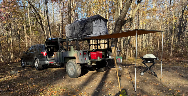 Overlanding setup with SUV, trailer, rooftop tent & awning. Great for an RV rental adventure in the woods.