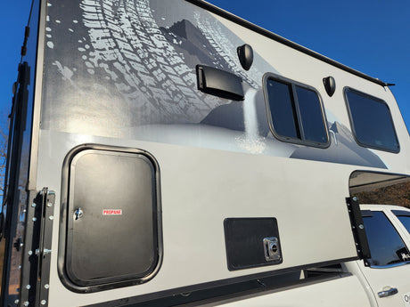 This RV rental features a truck camper with mountain graphics, propane access, and exterior amenities. Perfect for outdoor trips.