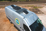Aerial view of a silver RV rental van with solar panels on its roof, parked near train tracks. Ideal for camper van adventures.
