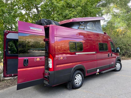 This maroon Winnebago Solis camper van, with open rear doors and a raised pop-top, is a perfect rv rental for outdoor adventures.