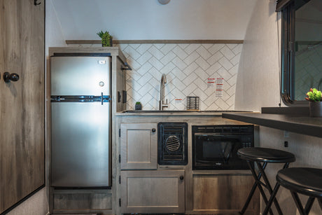 Modern RV rental kitchen showcasing a stainless fridge, sink, microwave, wood cabinets, herringbone backsplash, and a bar.