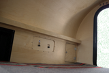 Inside an RV rental: Blonde wood interior with 'LIGHTS' & 'FAN PWR' controls, a small storage door, and cozy bedding.