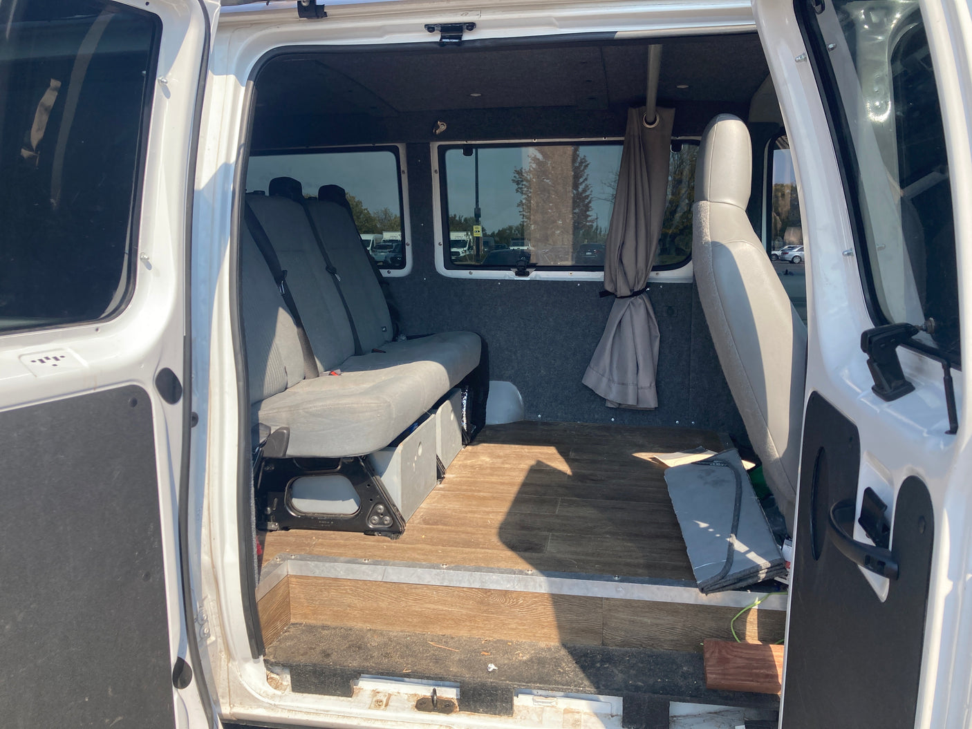 RV rental interior: A van's cozy cabin with bench seats, wood flooring, and privacy curtains, seen through the open side door.