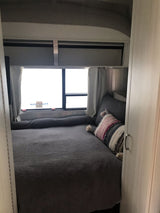 Cozy Airstream RV rental bedroom with gray bedding, a colorful pillow, and large windows. Ideal for travel.