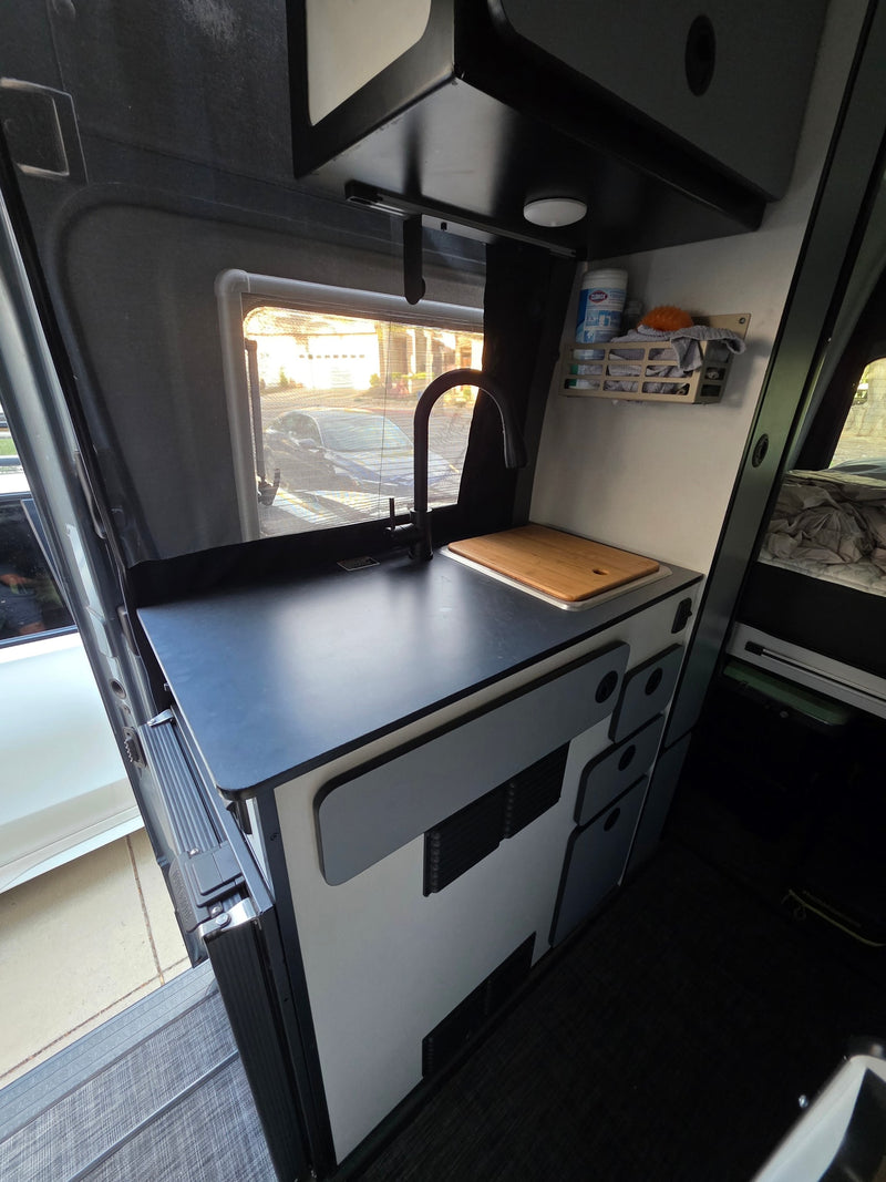 Modern RV rental interior: compact kitchen with black sink/faucet, smart storage, and outdoor view. — photo 7