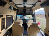 Spacious RV rental interior with comfortable tan captain's chairs, a media screen, and elegant overhead trim for luxury travel.