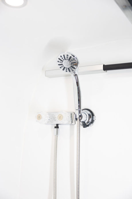 Compact shower in RV rental featuring chrome handheld showerhead and clear hot/cold knobs.