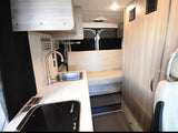 Compact RV rental interior featuring a modern kitchenette with sink, stovetop, and comfortable bench seating. Perfect for road trips.