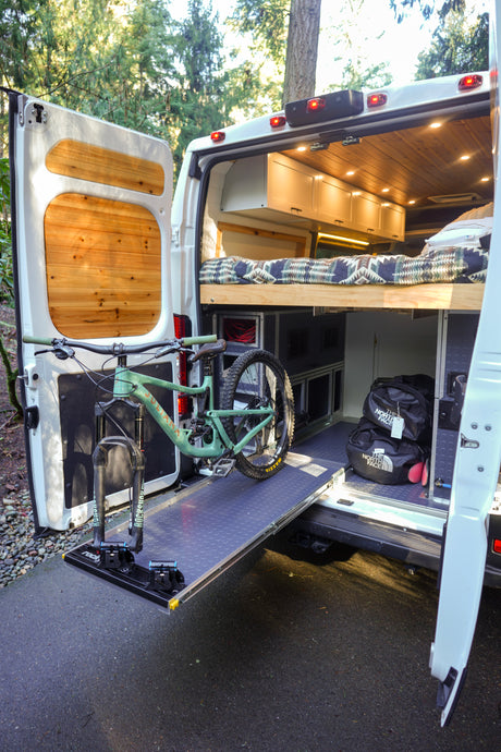 Custom rv rental van interior featuring a cozy bed, ample storage, and a mountain bike secured on a pull-out rack.