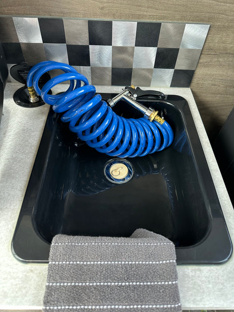 RV rental: A black utility sink with a blue coiled hose and spray nozzle. Non-potable water connection visible beside it, with a checkered backsplash.