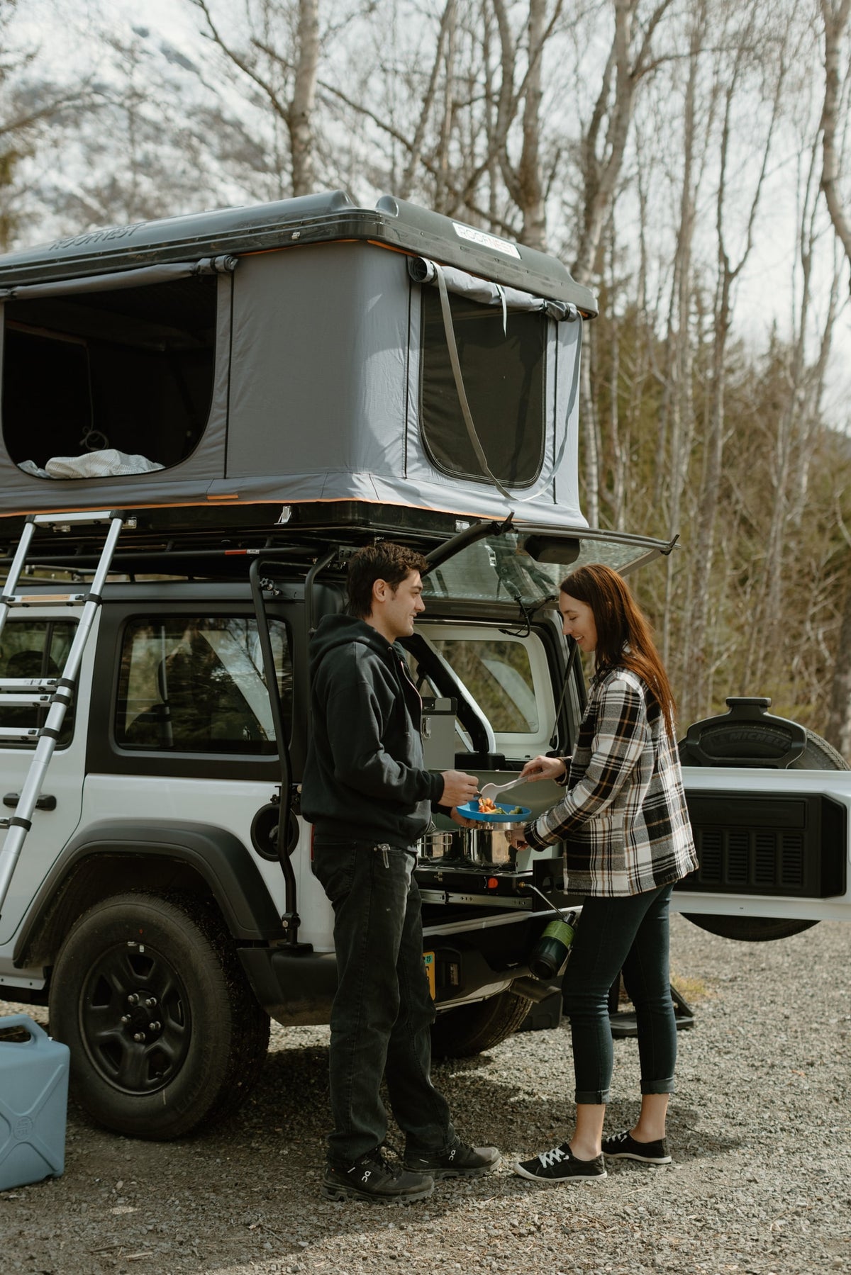 Couple cooks with a Roofnest rooftop tent on their RV rental, a compact camper setup for outdoor adventures. — photo 14